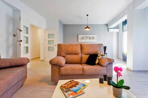 Una sala de estar moderna con un sofá, una mesa de centro con revistas, una planta en maceta y una lámpara colgante.