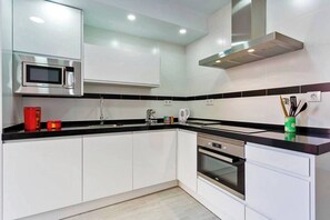 Eine moderne Küche mit weißen Schränken, einer schwarzen Arbeitsplatte, einer Mikrowelle, einem Backofen und einer Edelstahl-Dunstabzugshaube.