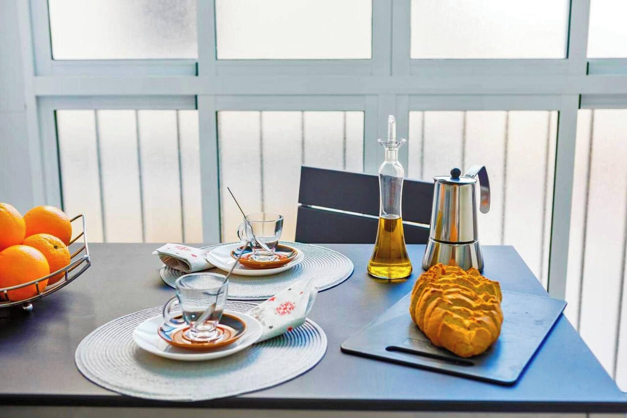 Ein Esstisch mit Orangen, einer Kaffeekanne, einer Ölflasche und einem Croissant.