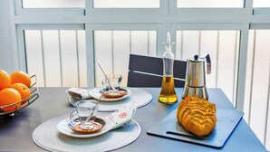 Mesa de café da manhã com laranjas, cafeteira, garrafa de azeite e croissant.