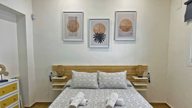 Un dormitorio ordenado con una cama, dos mesitas de noche, un tocador y tres obras de arte enmarcadas en la pared.