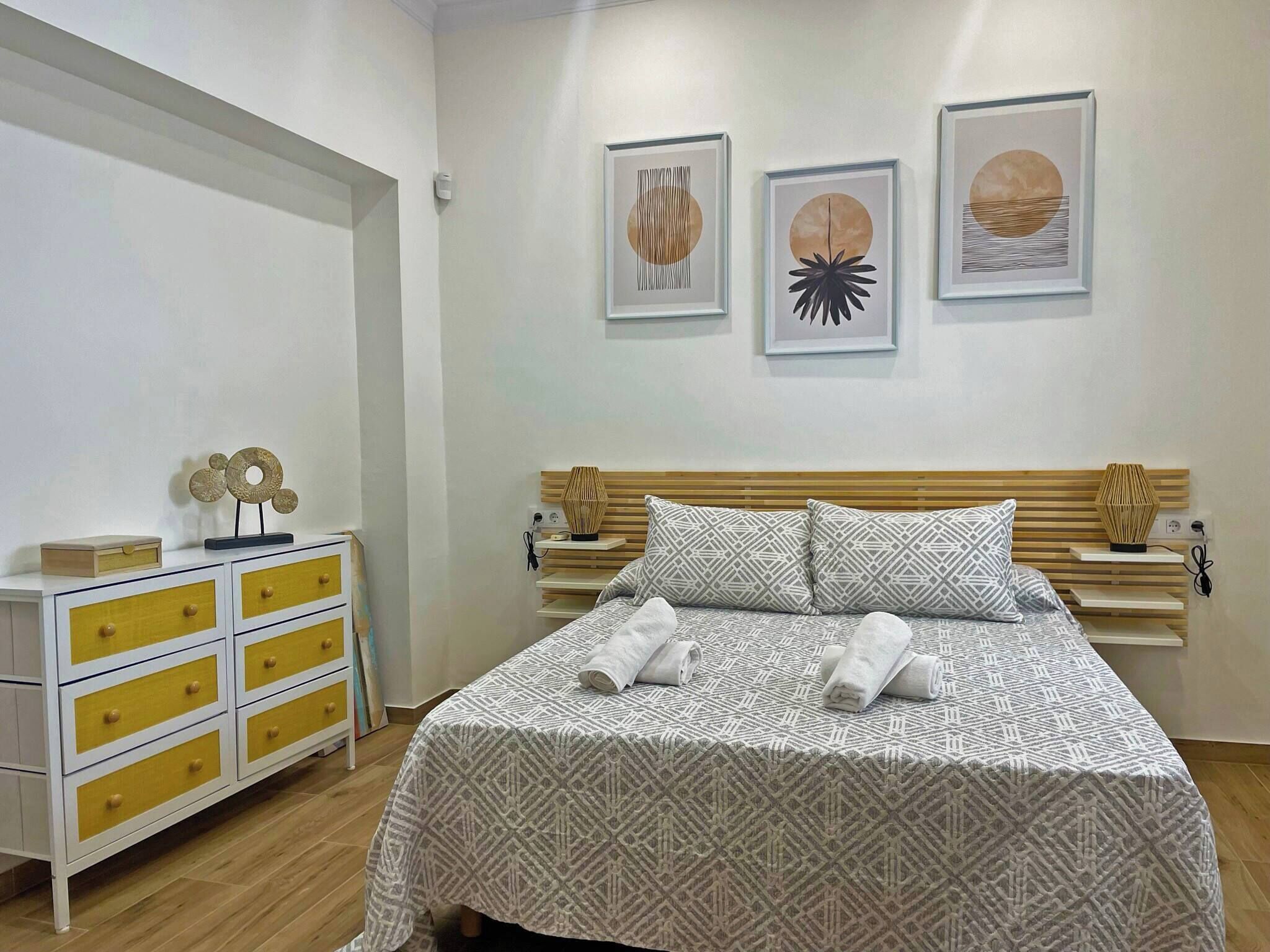 A bedroom with a bed, a nightstand, a dresser, and wall art.
