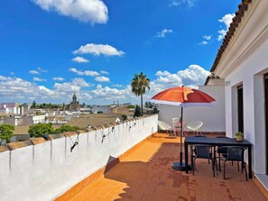 Una terrazza sul tetto con un tavolo e sedie, un ombrellone rosso e vista sulla città.
