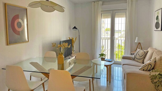 A modern living room with a glass dining table, white sofas, and a large window with curtains. - Apartamento El Carmen - Ole Solutions (Jerez de la Frontera)