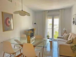 A modern living room with a glass dining table, white sofas, and a large window with curtains. - Apartamento El Carmen - Ole Solutions (Jerez de la Frontera)