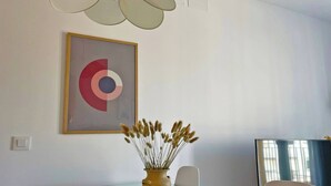 A modern meeting room with a glass table, a yellow vase with dried plants, a framed abstract artwork, and a ceiling fan. - Apartamento El Carmen - Ole Solutions (Jerez de la Frontera)