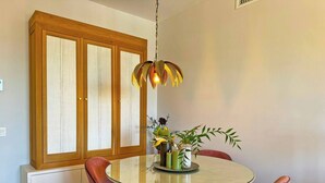 Un coin repas comprenant une table ronde, des chaises à revêtement rose, un buffet en bois doté de portes en verre et un luminaire suspendu.