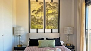 Un lit bien fait, avec des serviettes pliées, deux tables de chevet avec des lampes et un grand tableau représentant un paysage, accroché au-dessus du lit.