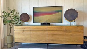Un salon moderne avec un téléviseur à écran plat fixé sur un meuble en bois, deux miroirs ronds décoratifs, une plante en pot et une table basse en marbre.