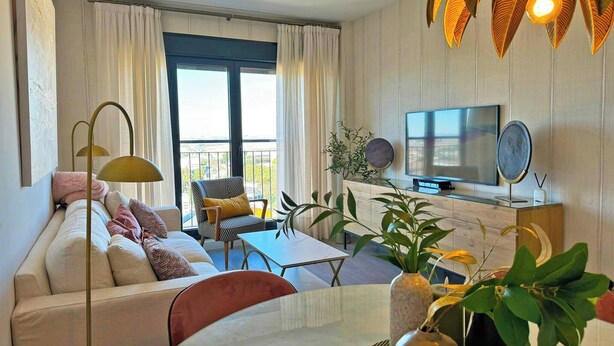 Un salon moderne avec un canapé, une table à manger, un téléviseur et de grandes fenêtres dotées de rideaux.