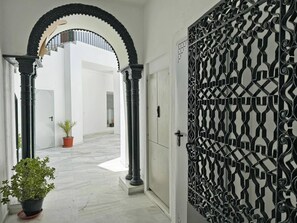 Un pasillo con paredes blancas, una reja de metal negro y una planta en maceta.