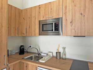 A modern kitchen with wooden cabinets, a stainless steel sink, a microwave, and a coffee maker.
