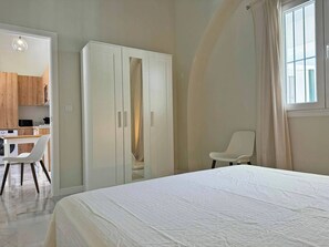 Un dormitorio con cama, armario, silla y vista a una cocina.