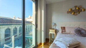 Una camera da letto con un'ampia finestra, un letto con cuscini, un comodino con una lampada e un'opera d'arte a parete.