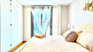 Una camera da letto con un letto grande, un armadio, una finestra con tende leggere e un comodino con una lampada.