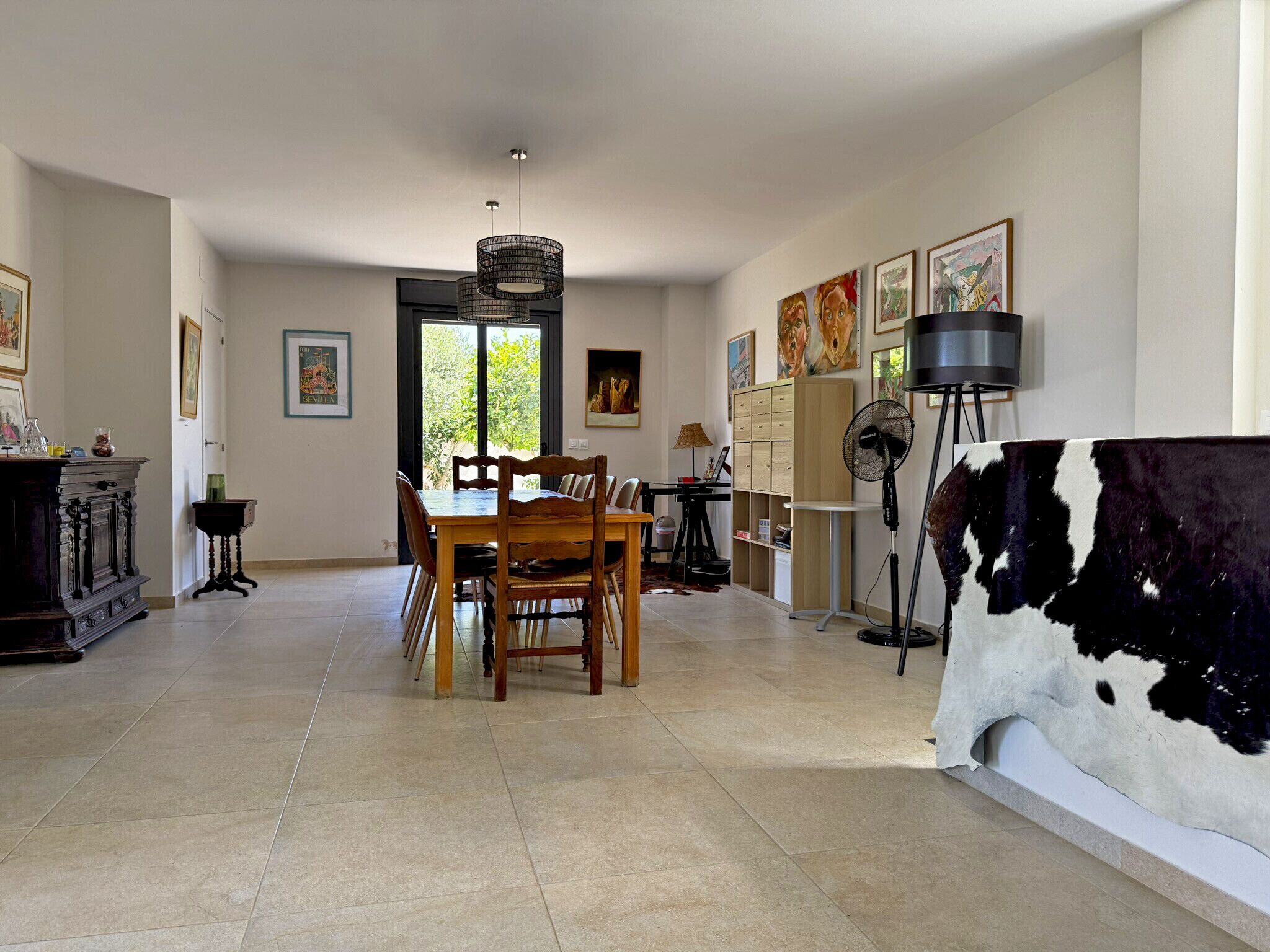 Un vaste espace dédié à la salle à manger, avec une table et des chaises en bois, un ventilateur de plafond et des œuvres d’art accrochées aux murs.