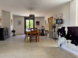 Un vaste espace dédié à la salle à manger, avec une table et des chaises en bois, un ventilateur de plafond et des œuvres d’art accrochées aux murs.