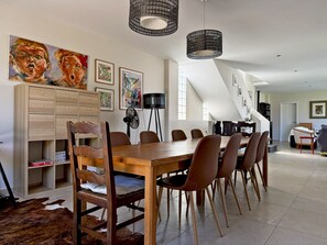 Een eetgedeelte met een houten tafel en stoelen, een ventilator en kunstwerken aan de muren.