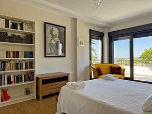 Une chambre avec un grand lit, une bibliothèque, un tableau encadré et un balcon avec vue.