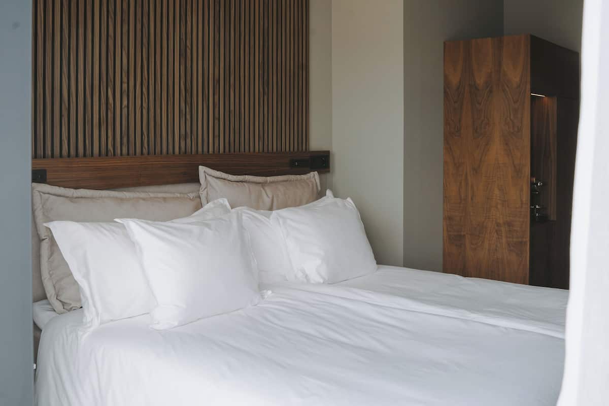A neatly made bed with white linens and a wooden headboard.