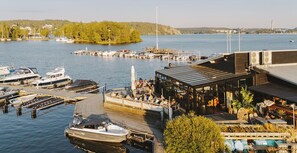 A marina with boats docked, a covered seating area, and a view of the water and distant land. - Season Hotel (Ekerö)