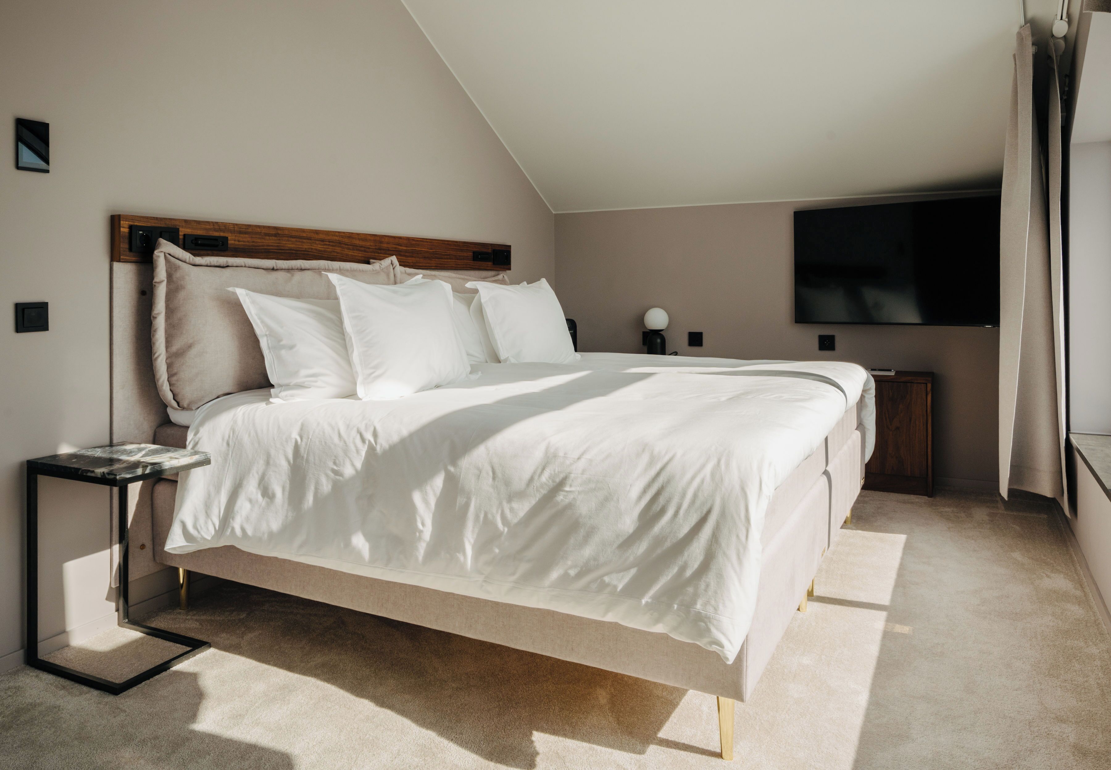 A modern bedroom with a large bed, a bedside table, a TV, and a window.