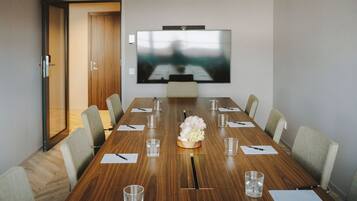 A conference room with a long wooden table, chairs, a TV screen, and a floral centerpiece.