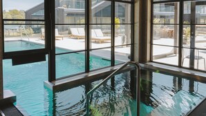 A swimming pool with a glass bottom, surrounded by lounge chairs and a modern building in the background. - Season Hotel (Ekerö)