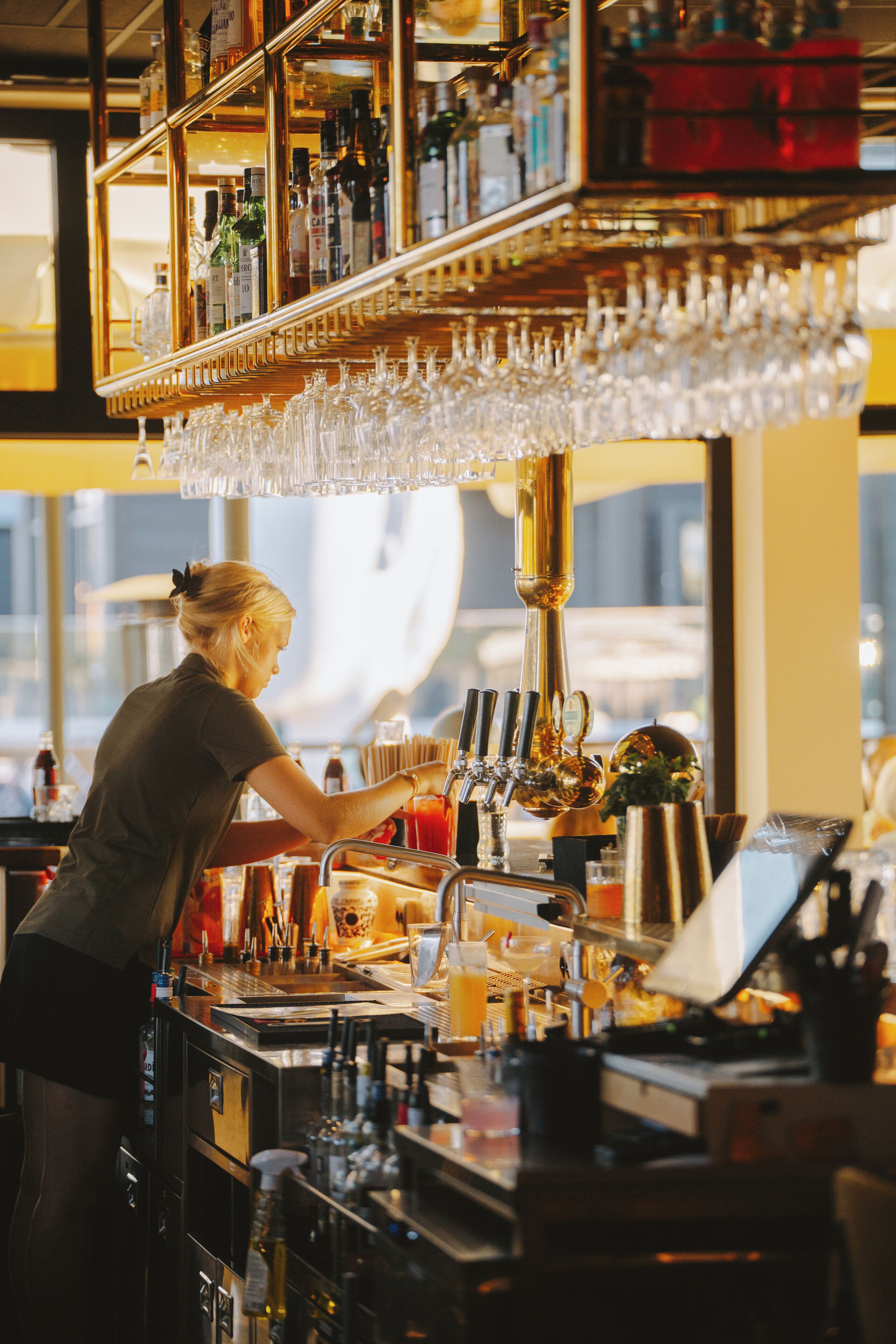 Zona de bar con un cantinero preparando bebidas, estanterías con botellas y una variedad de copas.