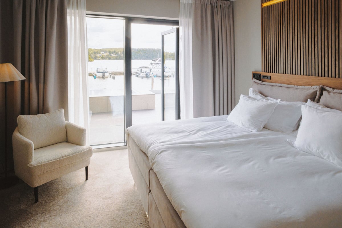 A hotel room with a large bed, a chair, and a view of a body of water through a sliding glass door.