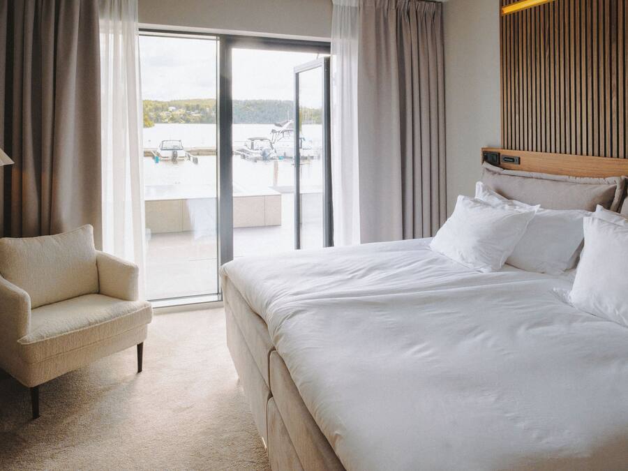 A hotel room with a large bed, a chair, and a view of a body of water through a sliding glass door.