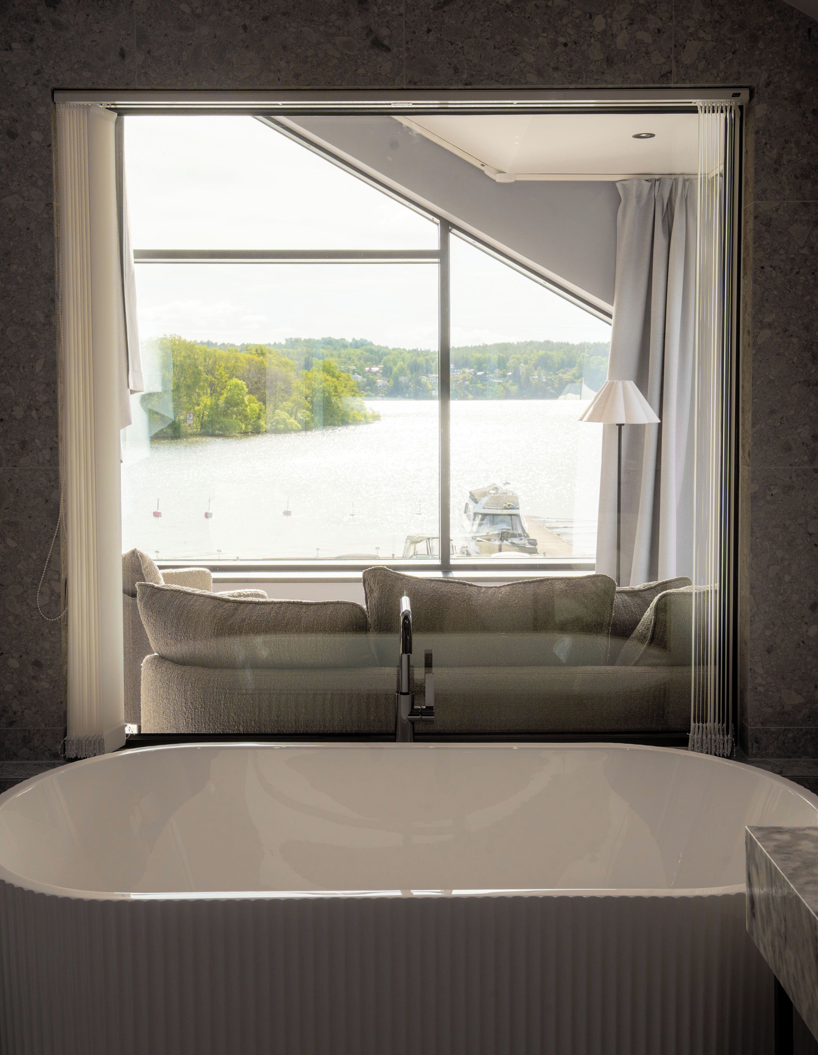 A modern bathroom with a large bathtub, a window with a view of a lake, and a sofa by the window.