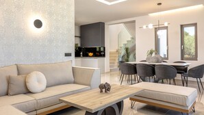 A modern living room with a sofa, a coffee table, and a dining area with chairs. - Villa Frantzeska (Zakynthos)