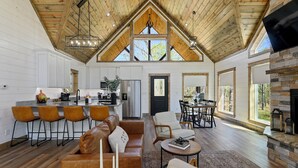 A spacious loft-style living area with a high ceiling, wooden beams, a fireplace, and large windows.