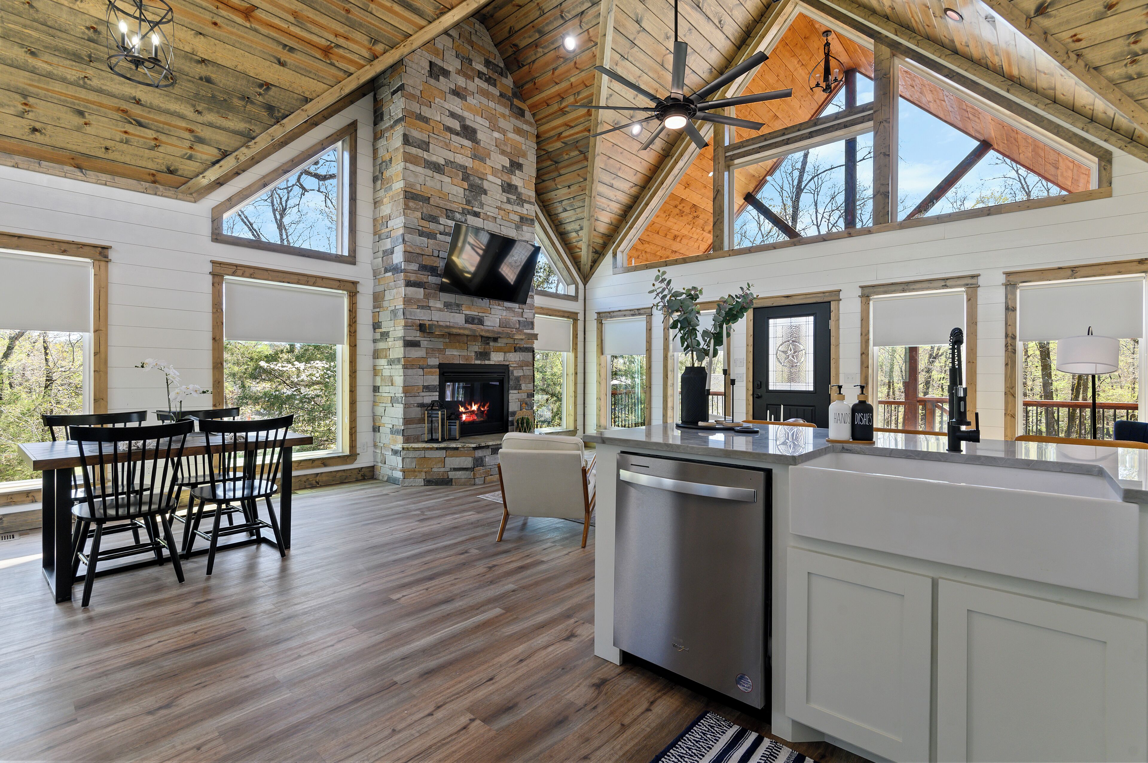 A spacious kitchen with a stone fireplace, wooden ceiling, and large windows.