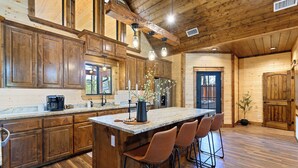A spacious kitchen with wooden cabinets, a large island with bar stools, and a view of the outdoors. - The Hickory Nut | 2 Bed | 2.5 Bath | Sleeps 4 (Broken Bow)