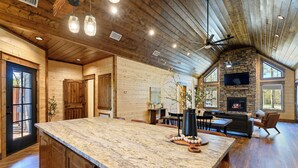 A spacious kitchen with a large island, wooden walls, and a stone fireplace. - The Hickory Nut | 2 Bed | 2.5 Bath | Sleeps 4 (Broken Bow)
