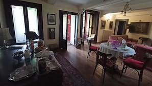 A dining area with a round table, chairs, and a red sofa. There is a window with curtains, a chandelier, and a door leading to another room. - Foresteria Lombarda B & B Cà Pelitti - Room with French bed (Ganna)
