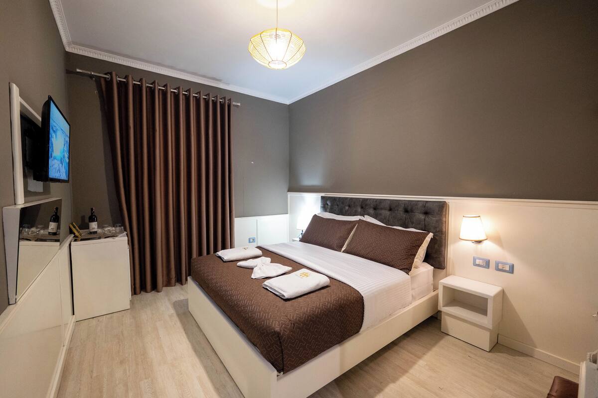 A modern hotel room with a large bed, a television, a minibar, and a nightstand with a lamp.