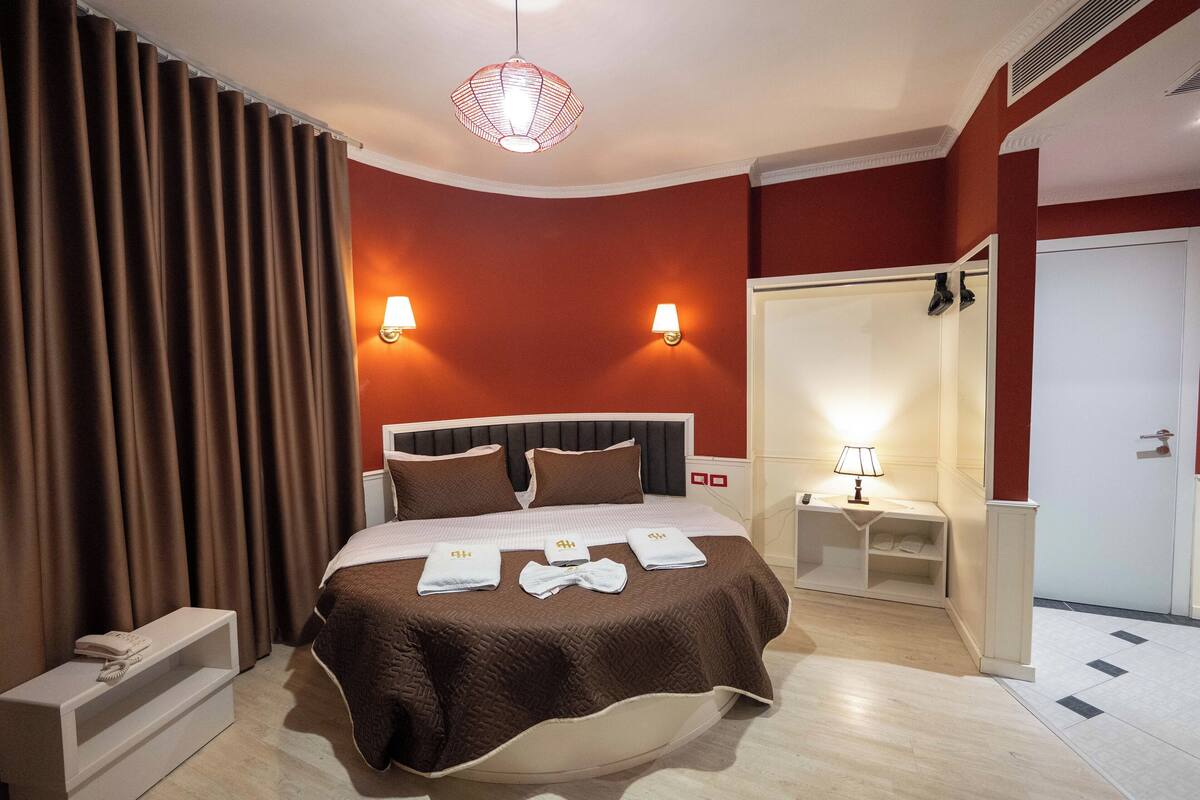 A hotel room with a large bed, two bedside lamps, a wardrobe, a nightstand, and a mirror.