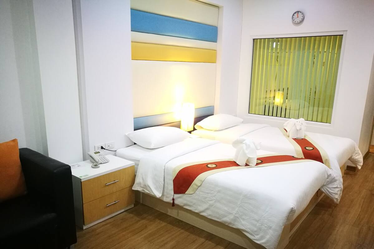 Una habitación de hotel con cama, mesita de noche, lámpara y ventana con persianas.