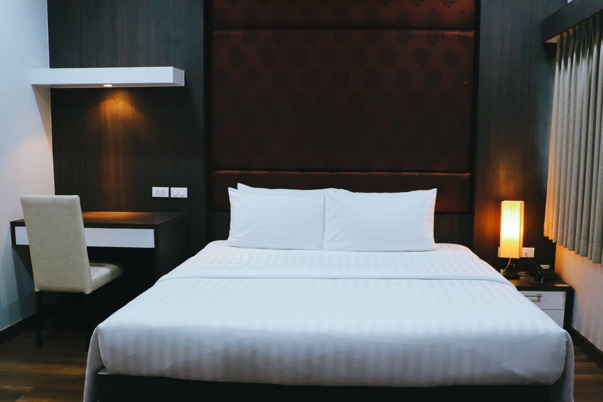Habitación de hotel con una cama grande, un escritorio, una silla, una mesita de noche con lámpara y un cabecero.