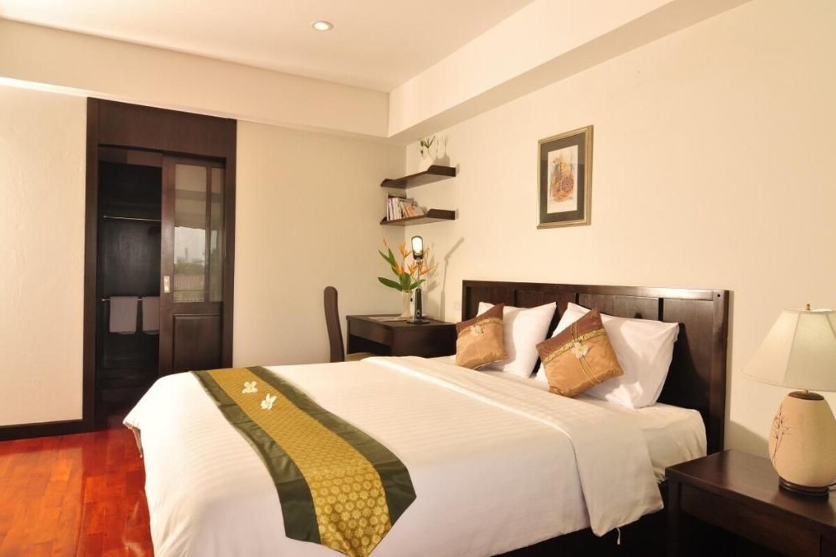 Una habitación de hotel con cama, mesita de noche, lámpara y puerta que da a un balcón.