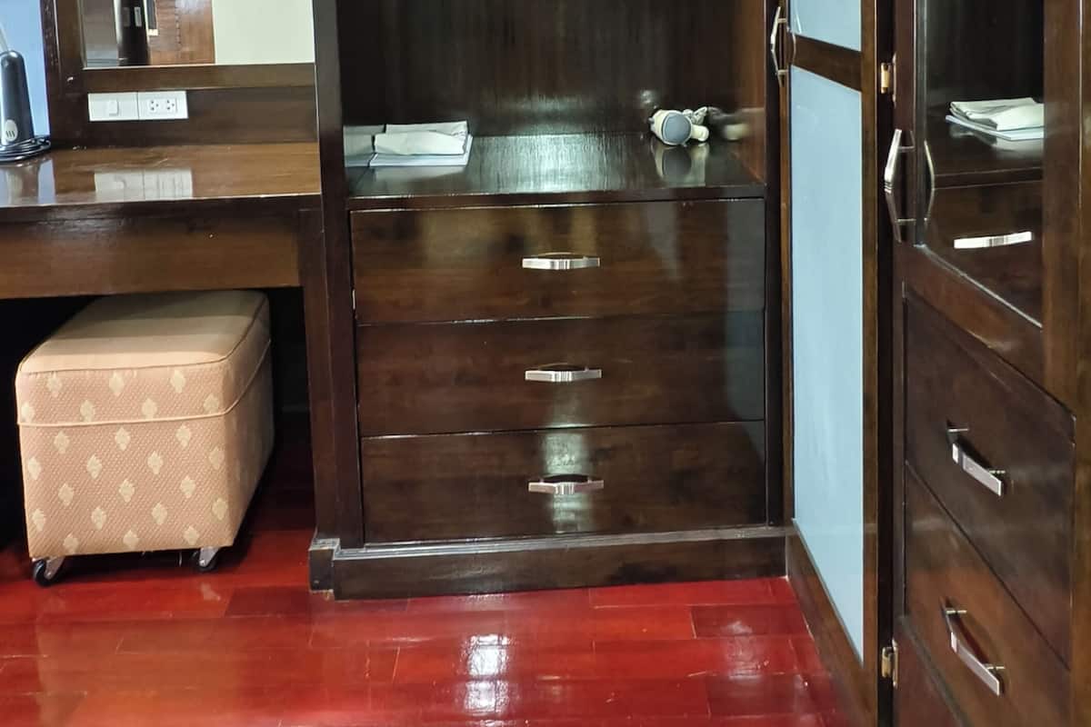 Una habitación con un armario de madera, un espejo, un pequeño taburete beige y un suelo de baldosas rojas.