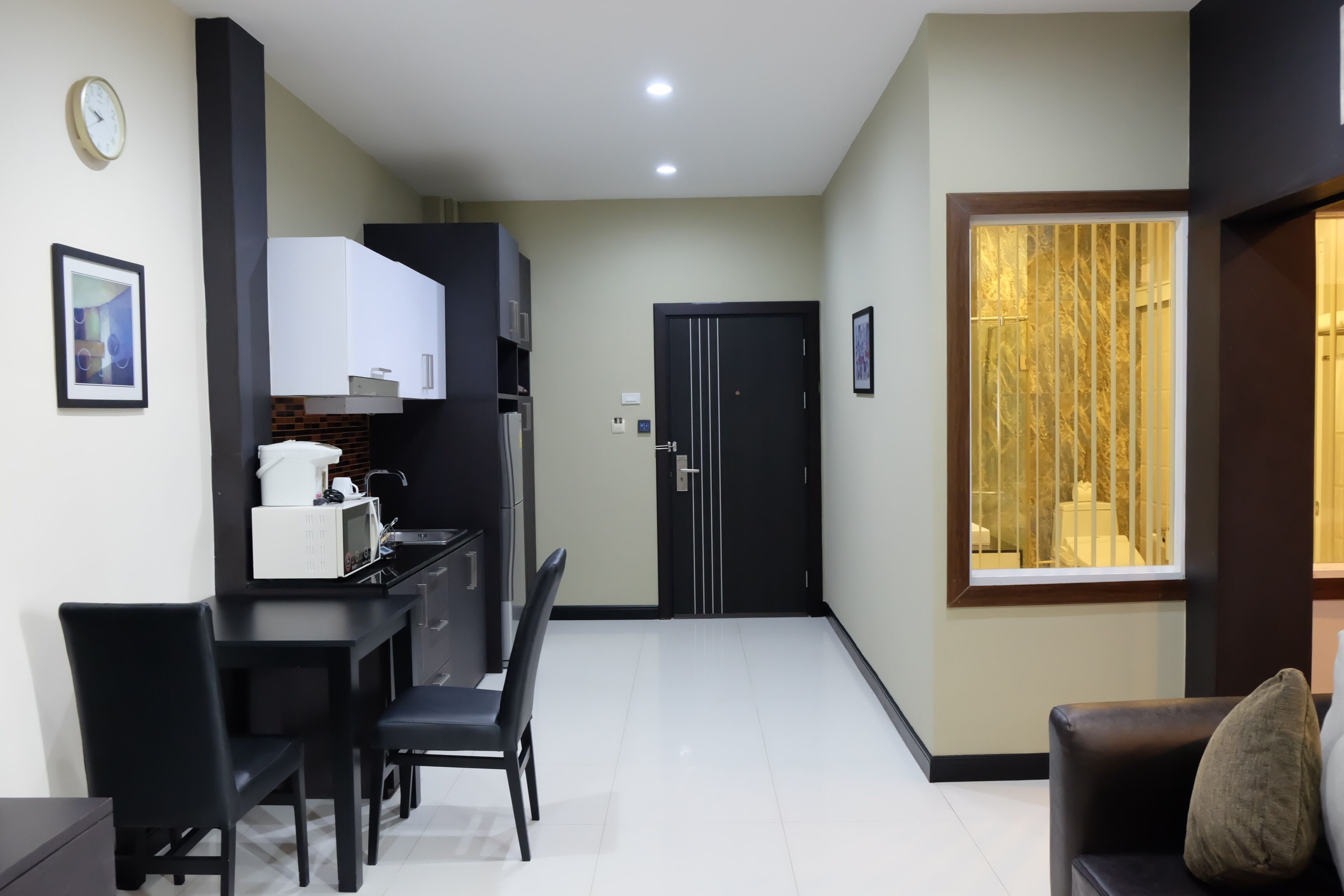 A modern kitchen with white cabinets, a microwave, and a dining area with black chairs.