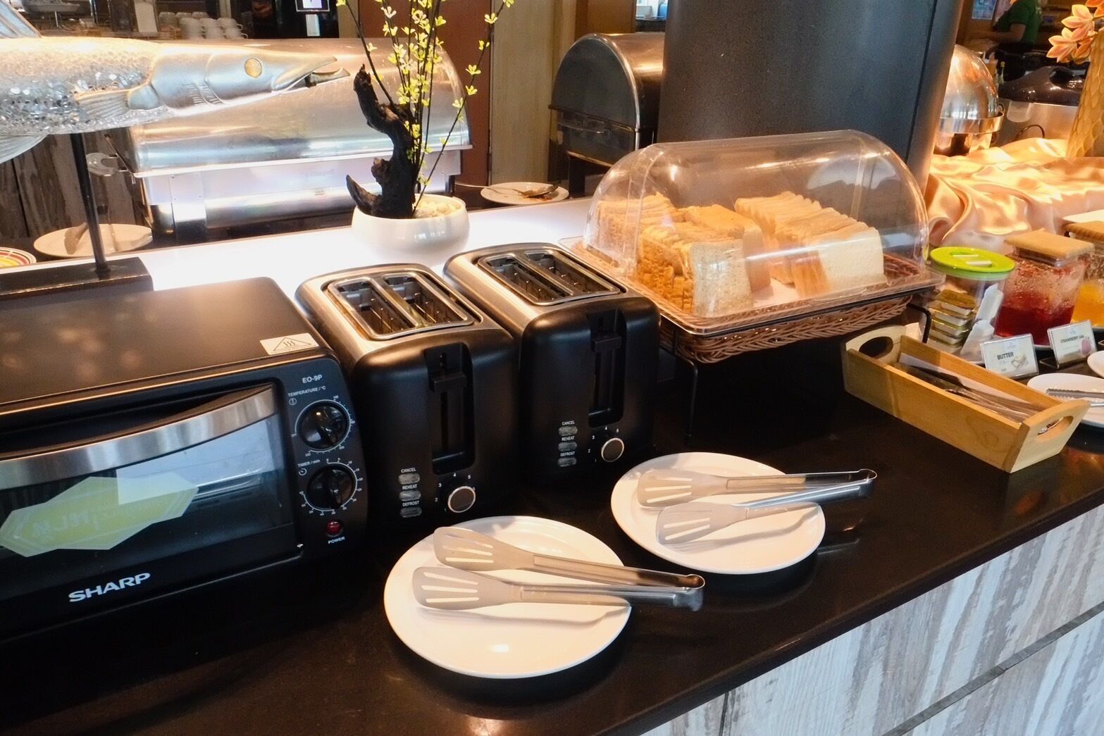 A breakfast buffet setup with toasters, a microwave, and plates with utensils.