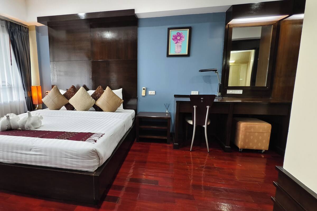 Habitación de hotel con una cama grande, un escritorio, una silla, un espejo y una ventana con cortinas.