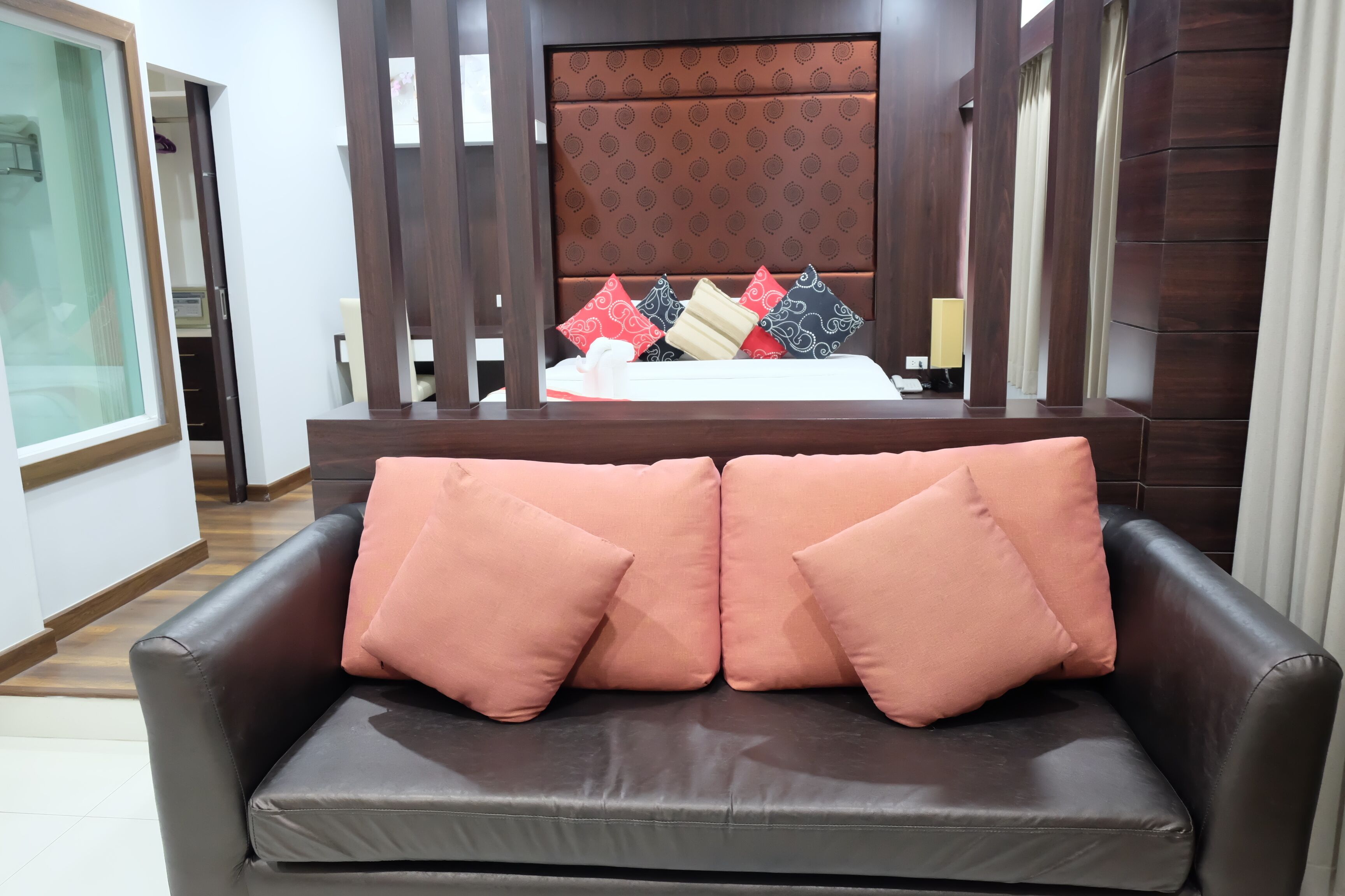 A hotel room with a bed, a wooden headboard, and a brown leather sofa with pink cushions.
