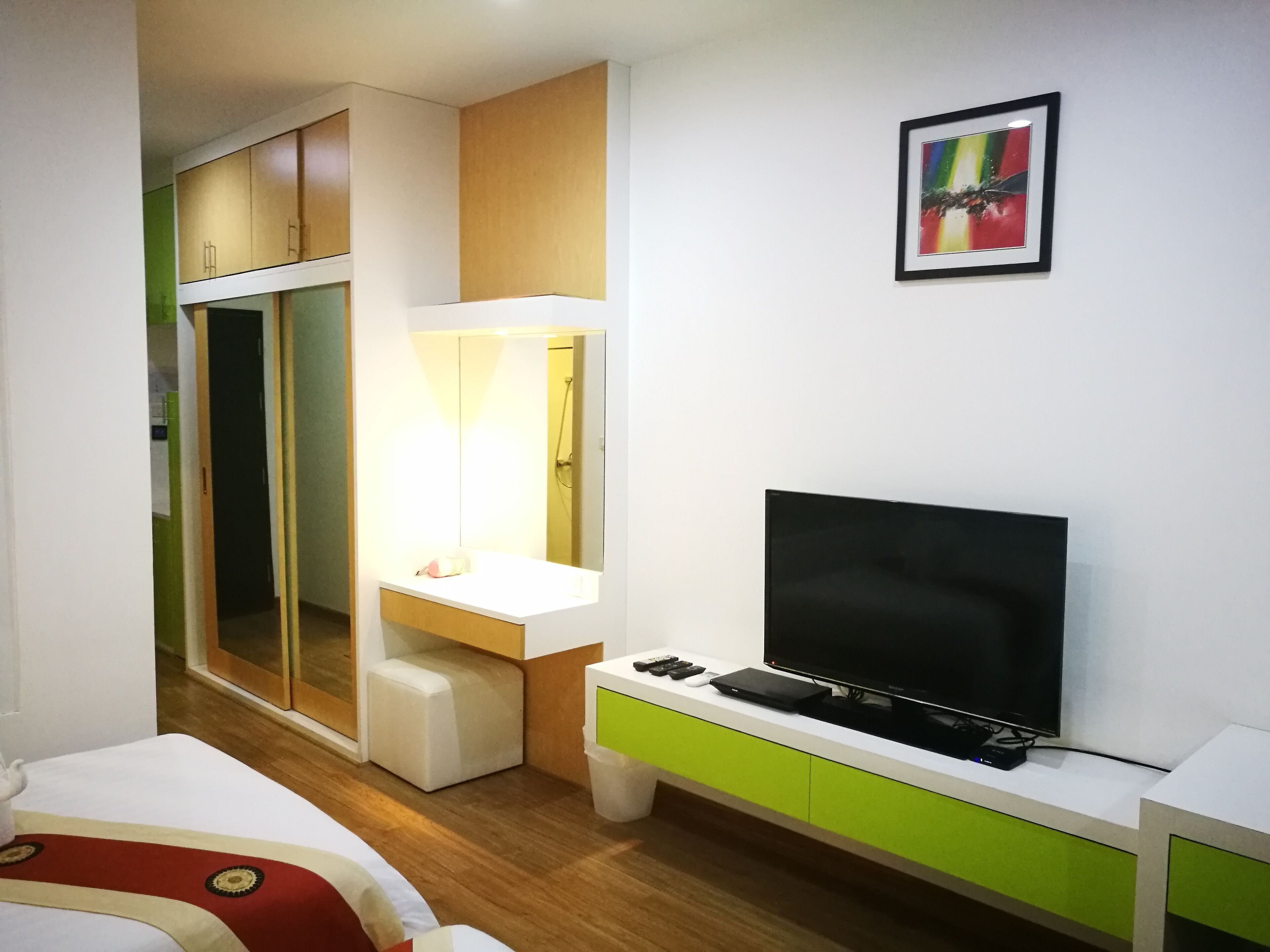 A modern hotel room with a bed, a TV, a desk with a mirror, and a wardrobe.