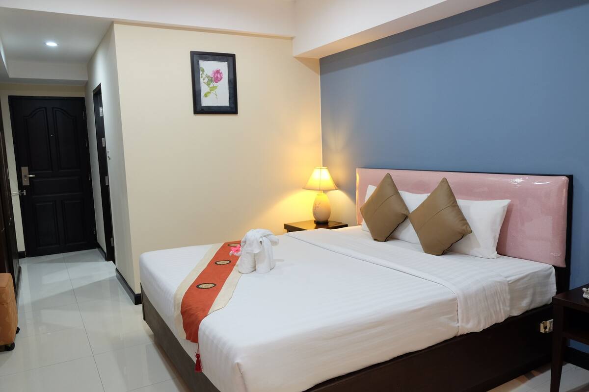 Una habitación de hotel con una cama, una mesita de noche, una lámpara, un cuadro en la pared y una puerta.